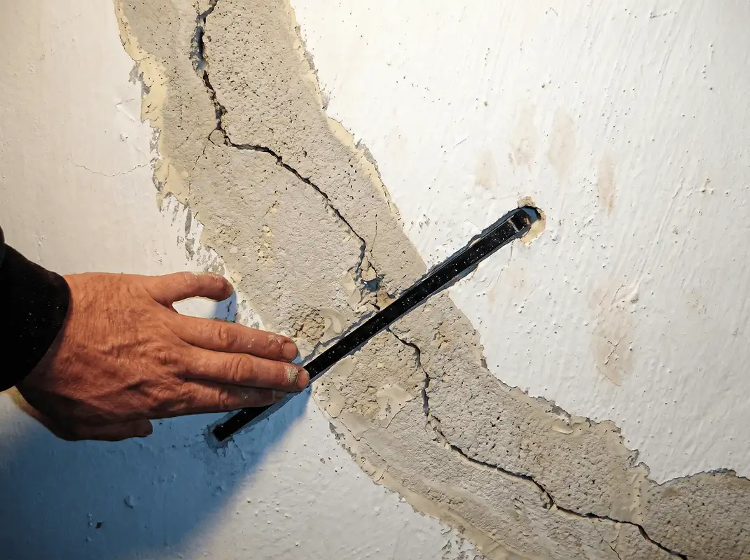A wall with a large crack is being inspected by a professional in Baltimore, MD